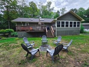 A house with a deck, a fire pit, and outdoor seating. - Forest Edge Burrow - Wooded Yard, Hot Tub, with Long Lake Access (Traverse City)