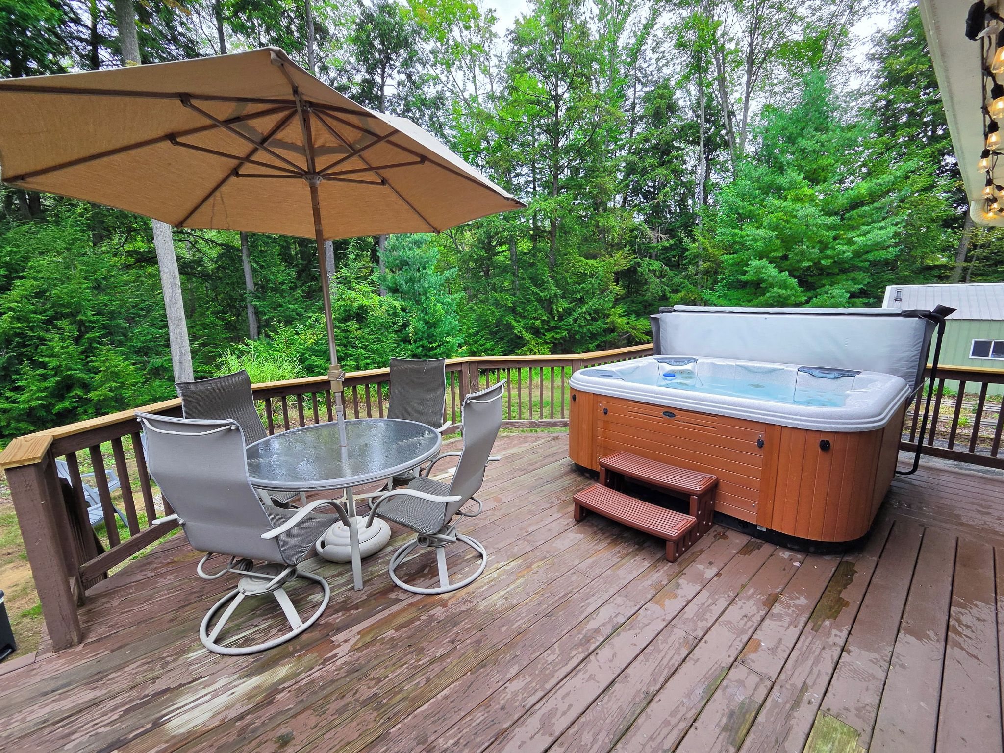 A wooden deck with a hot tub, a table with chairs, and an umbrella.