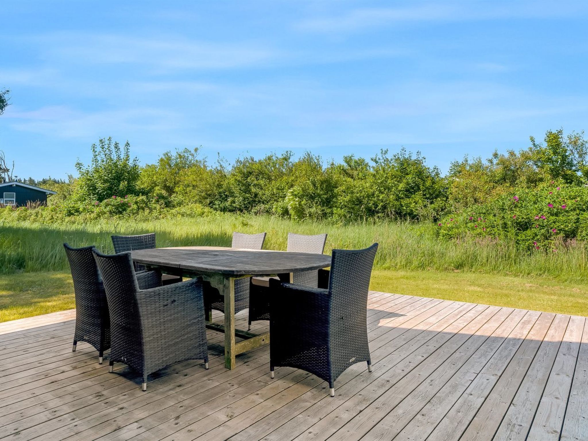 En udendørs træterrasse med et bord og stole.