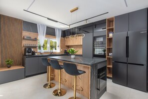 A modern kitchen with a central island, bar stools, a built-in oven, and a large refrigerator. - NEW! Luxurious Villa River Rose: Heated Pool, Jacuzzi, 4 En-Suite Bedrooms (Dugopolje)