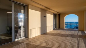 Een balkon met uitzicht op zee, een glazen deur en een betegelde vloer.