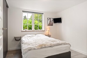 Ein Schlafzimmer mit einem Bett, einem Fenster, einem an der Wand montierten Fernseher und einer Nachttischlampe.