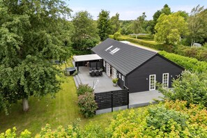 Ein schwarzes Haus mit einer Terrasse, umgeben von viel Grün.