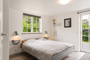 A bedroom with a bed, two bedside lamps, a window, a mirror, and a door leading to an outdoor area. - Modern holiday home with hot tub and nature (Vig)