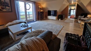 Ein geräumiges Wohnzimmer mit Fernseher, Kamin, Essbereich und Blick ins Freie.