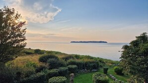 Eine Küstenlandschaft mit einer Rasenfläche, ordentlich gestutzten Büschen und Blick auf das Meer und das entfernte Land.