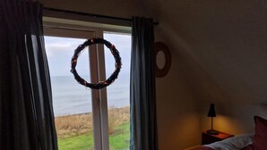 Ein Schlafzimmer mit Bett, Nachttisch, Lampe, Blick ins Freie und einem Kranz am Fenster.