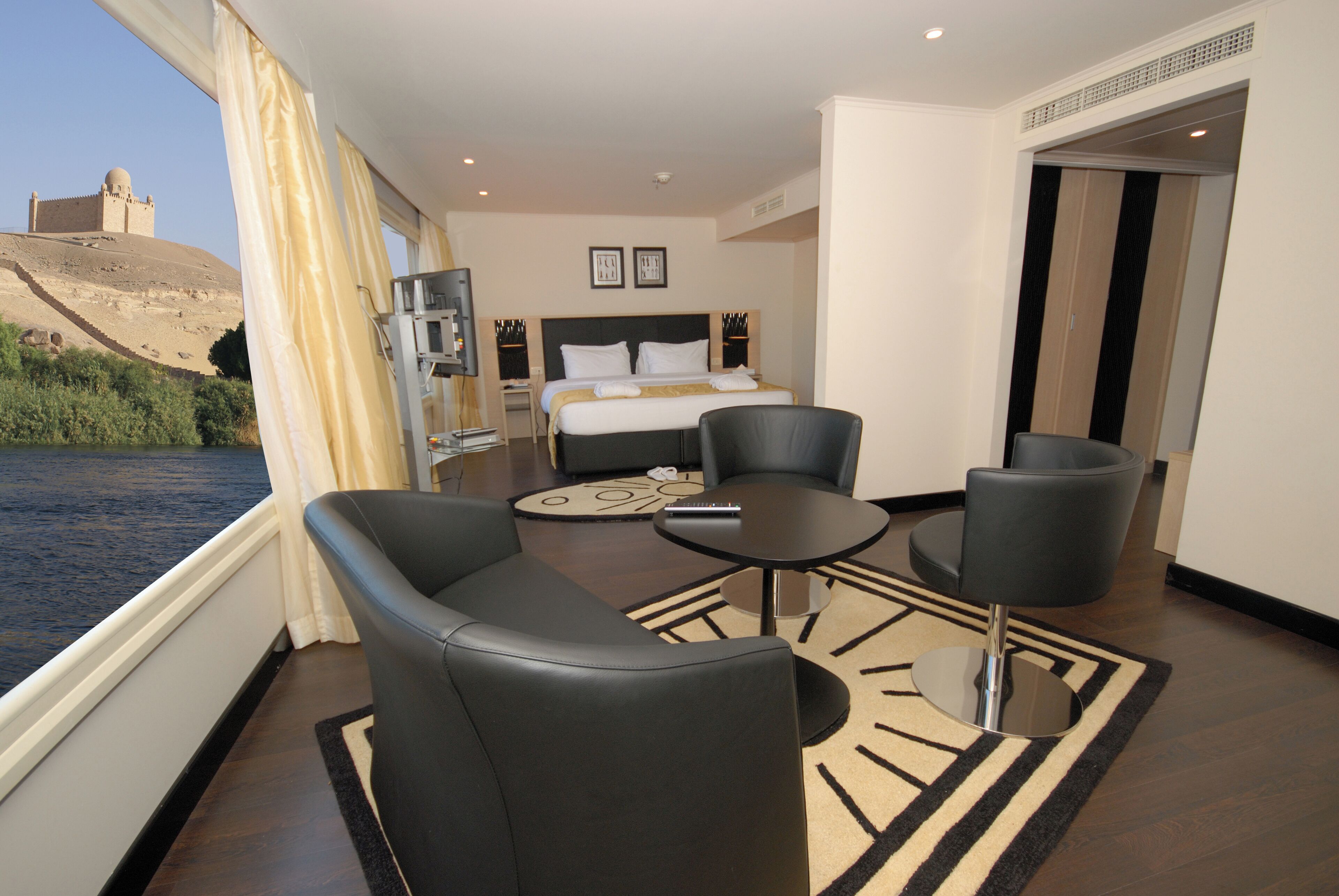 Habitación de hotel con cama, dos sillones, una mesita y vistas a un cuerpo de agua y una colina.