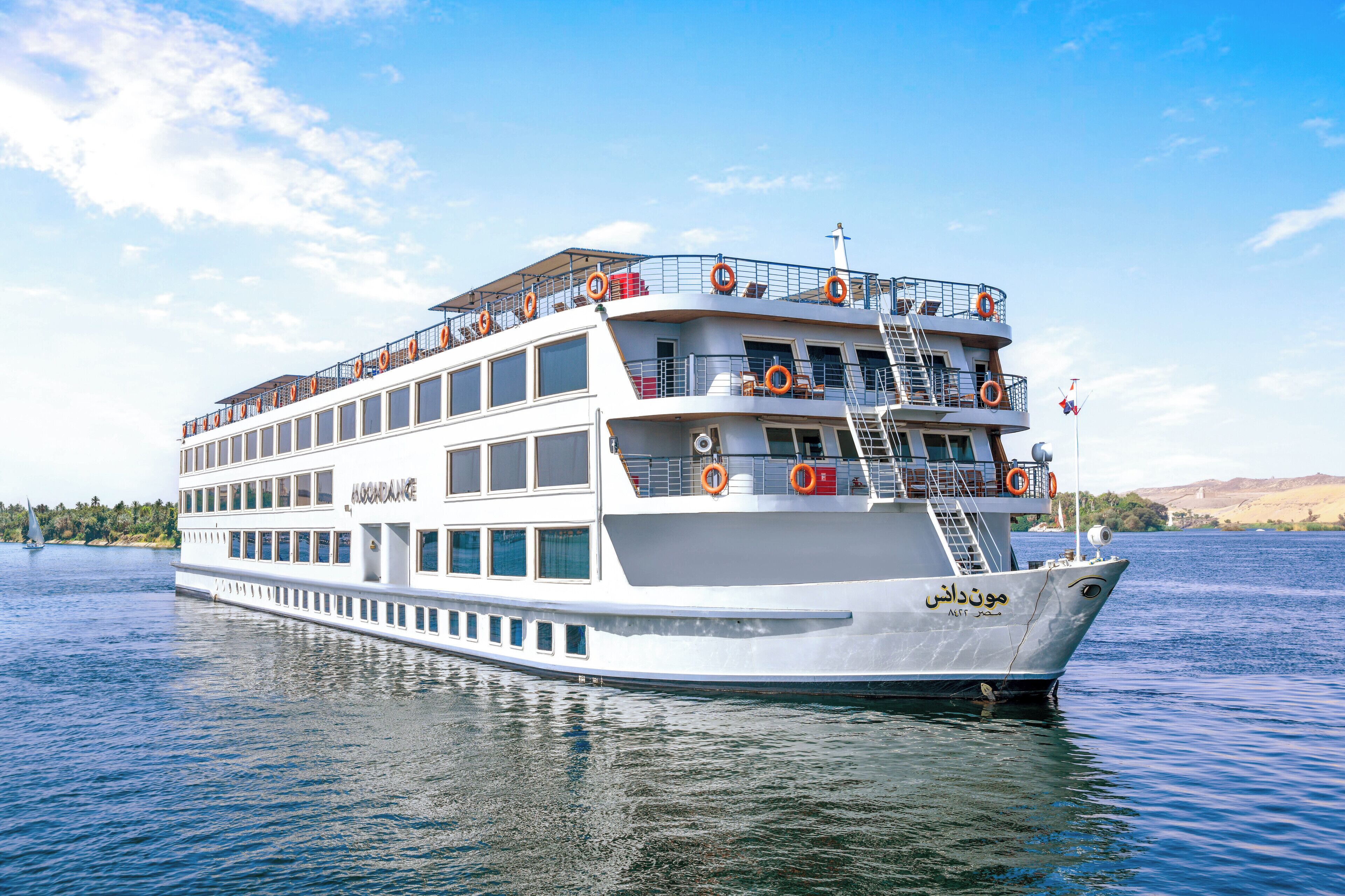 A large, multi-deck river cruise ship with lifeboats on the upper deck and a clear view of the river.
