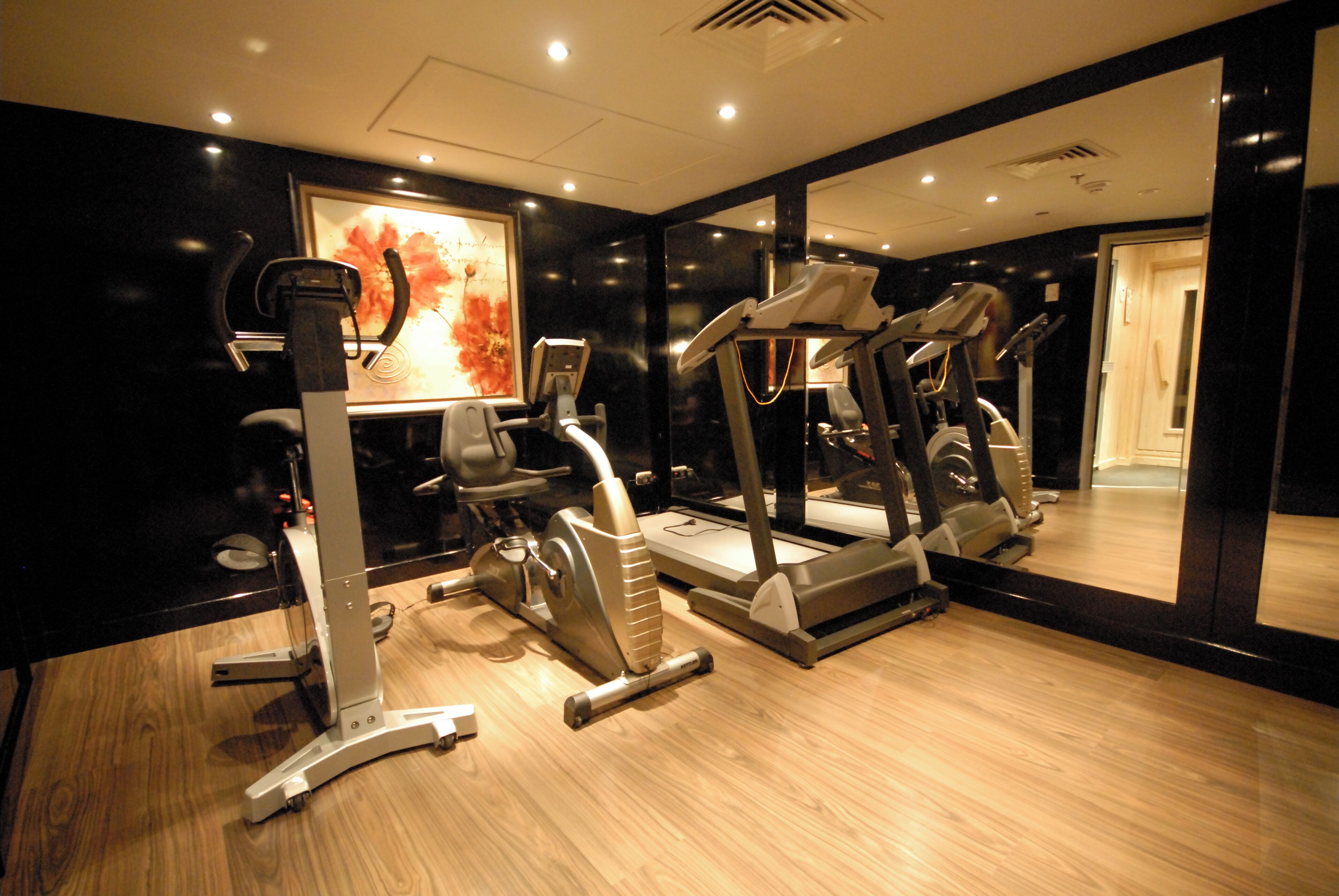 A gym with cardio machines, a mirror, and a wooden floor.