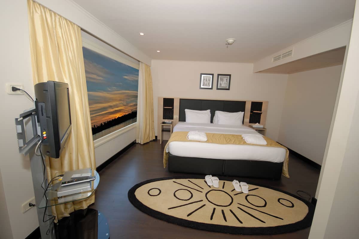 A hotel room with a bed, a TV, a desk, and a window with a sunset view.