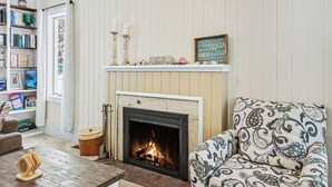 A cozy living room with a fireplace, a bookshelf, and a patterned armchair. - Retreat with fire pit, walking distance to beach (Douglas)