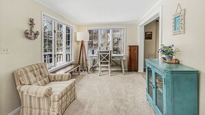 A room with a striped armchair, a desk with a chair, a cabinet, and large windows. - Retreat with fire pit, walking distance to beach (Douglas)