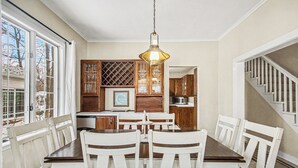 A dining area with a wooden table and white chairs, a hanging light fixture, and wooden cabinets. - Retreat with fire pit, walking distance to beach (Douglas)