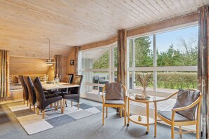 Et træpanelt interiør med et spiseområde, stole, et bord og store vinduer.