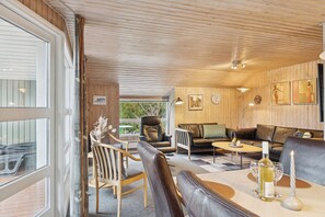En hyggelig indretning med træloft, en sofa, et spisebord med flaske og glas samt en stol med en vase.