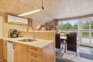 A kitchen with wooden cabinets, a sink, and a dining area with a table and chairs. - Holiday home with spa sauna and nature (Nørre Nebel)