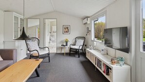 Et værelse med et fjernsyn, to stole, et bord, en bogreol og et vindue.