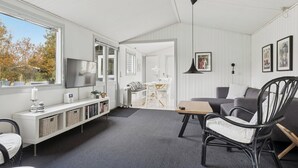En moderne stue med TV, siddepladser, et spiseområde og udsigt gennem vinduet.