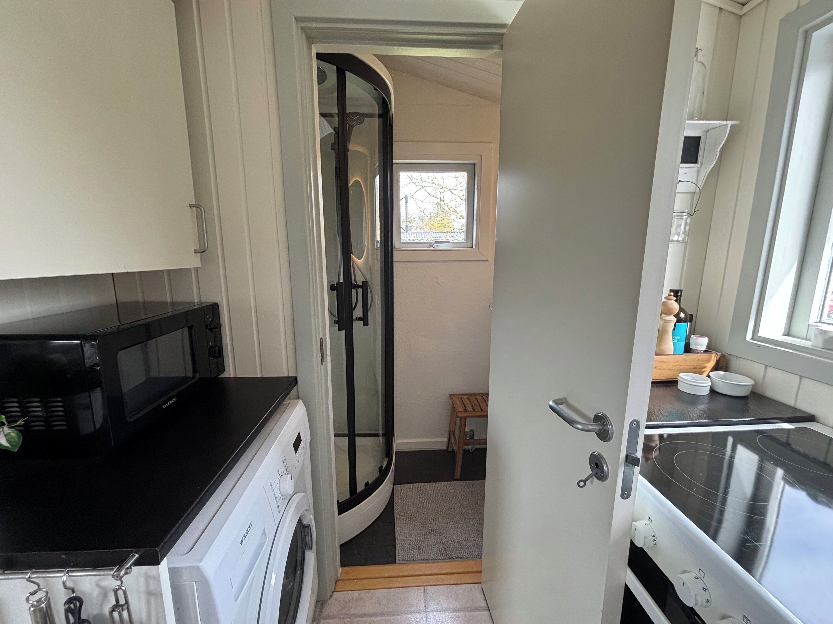 A compact kitchen with a microwave, oven, and a glass shower door.