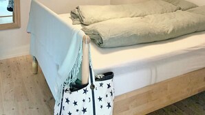 Un dormitorio con cama, lámpara colgante, mesita de noche y ventana.