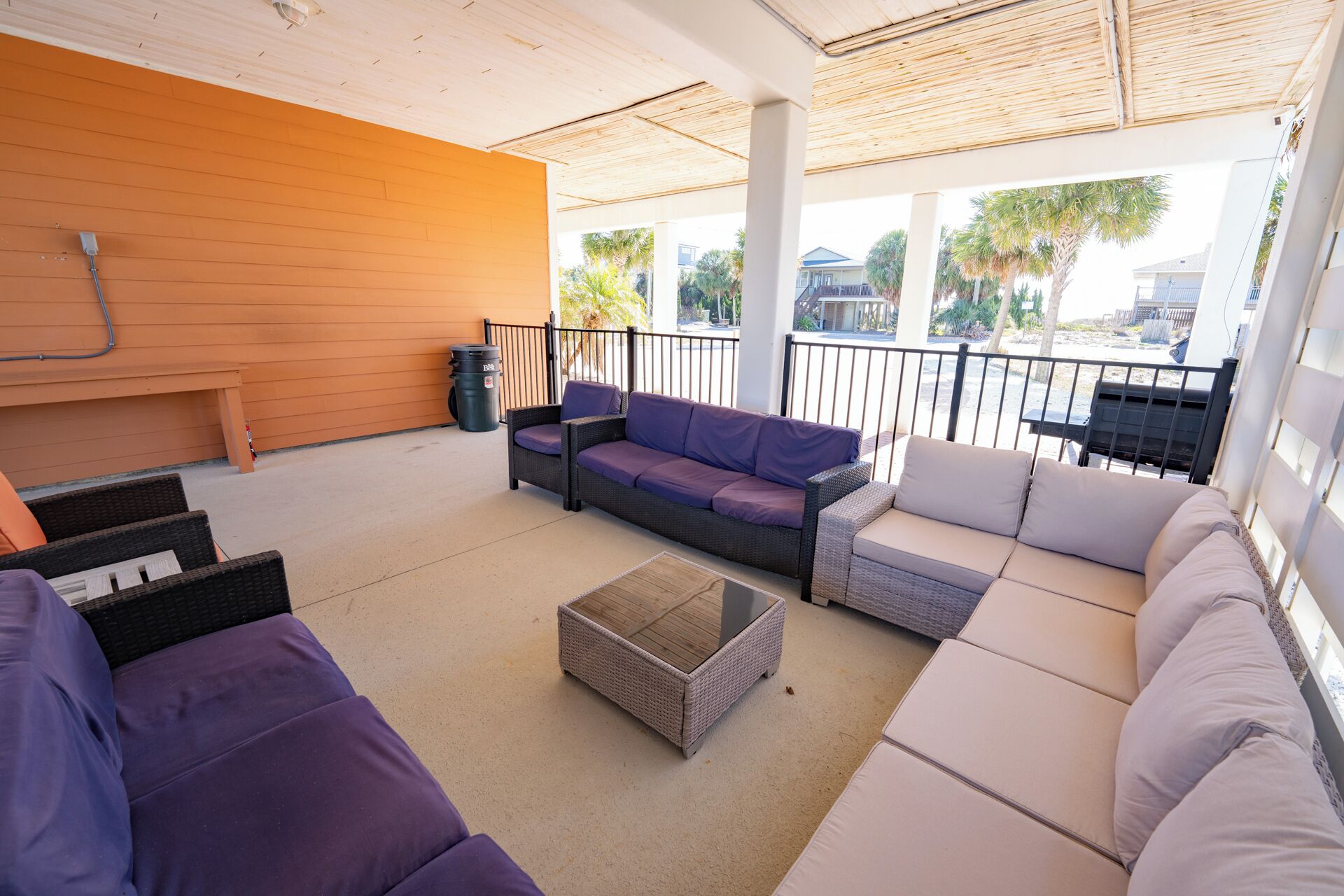 A covered outdoor seating area with wicker furniture and a trash bin.