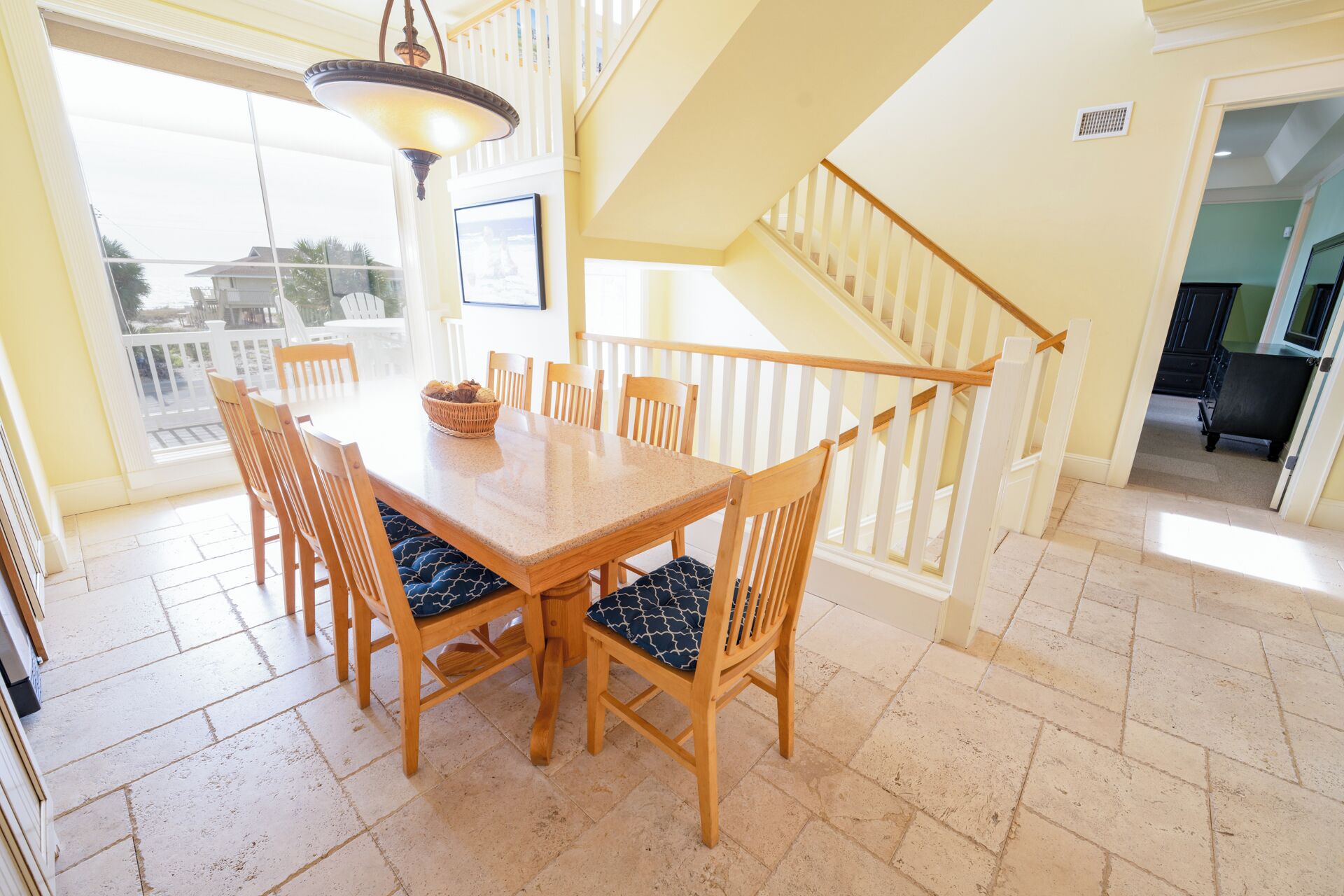 A dining area with a wooden table and chairs, a chandelier, and a staircase leading to an upper level.