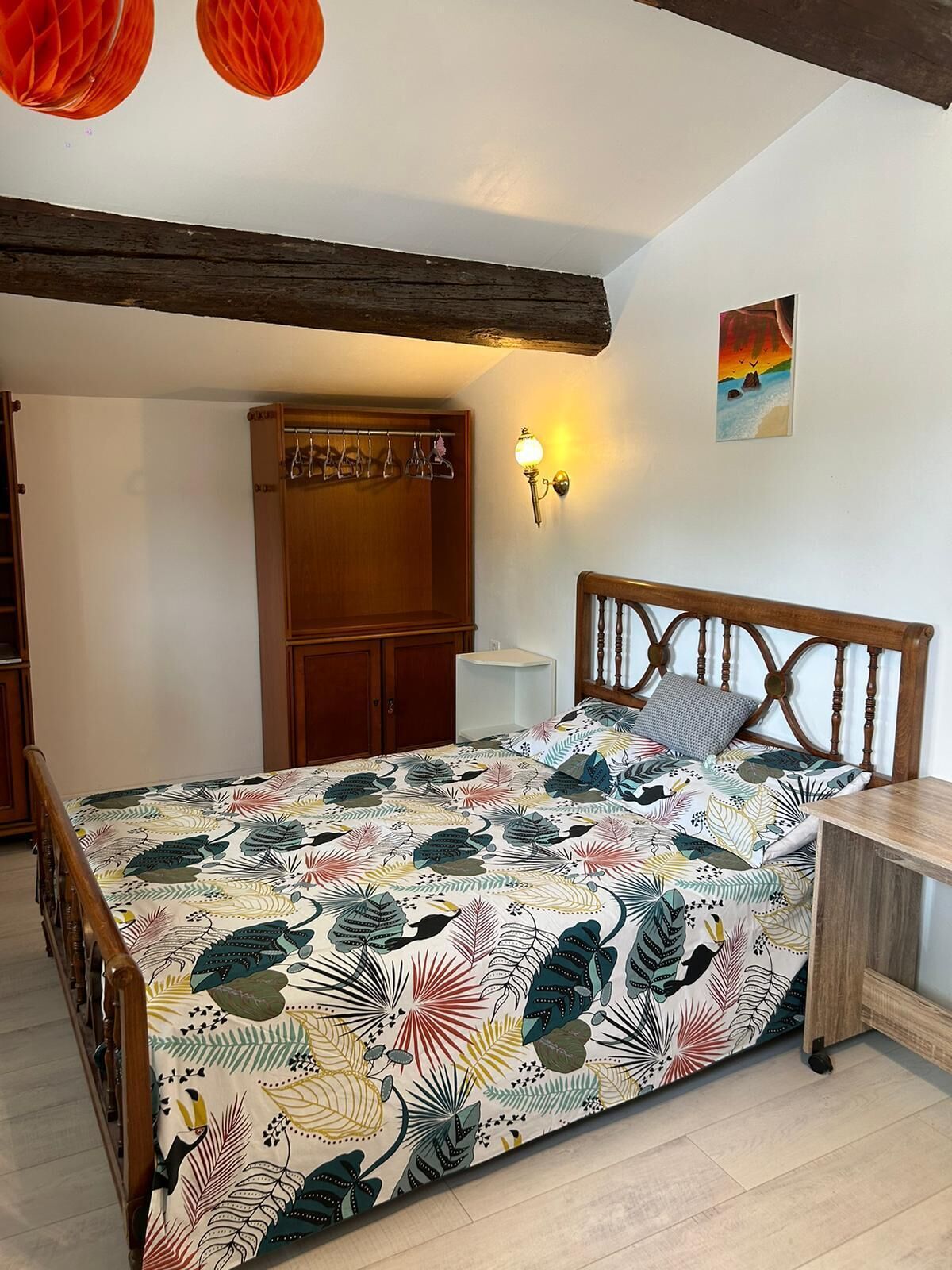 A bedroom with a bed, wooden headboard, a nightstand, a wardrobe, and a wall-mounted lamp.