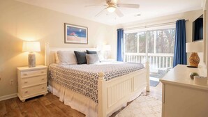 Ein Schlafzimmer mit einem Bett, Nachttischen, einem Schreibtisch, einem Deckenventilator und einem Fenster mit Vorhängen.