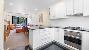 Een moderne keuken met witte kastjes, een roestvrijstalen oven en een zithoek met een bank en stoelen.