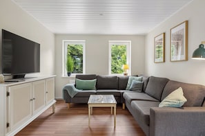 A living room with a sectional sofa, a flat-screen TV, a glass coffee table, and a cabinet.