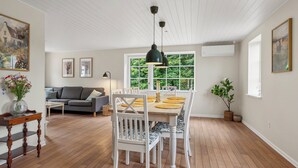 Un coin repas avec une table en bois, des chaises blanches et un luminaire suspendu.