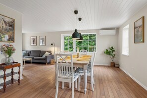 Un comedor con mesa de madera, sillas blancas y una lámpara colgante.