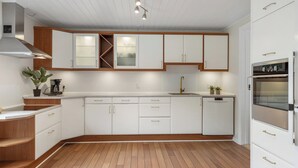 Une cuisine moderne avec des armoires blanches, un plancher en bois, un four encastré et un réfrigérateur en acier inoxydable.