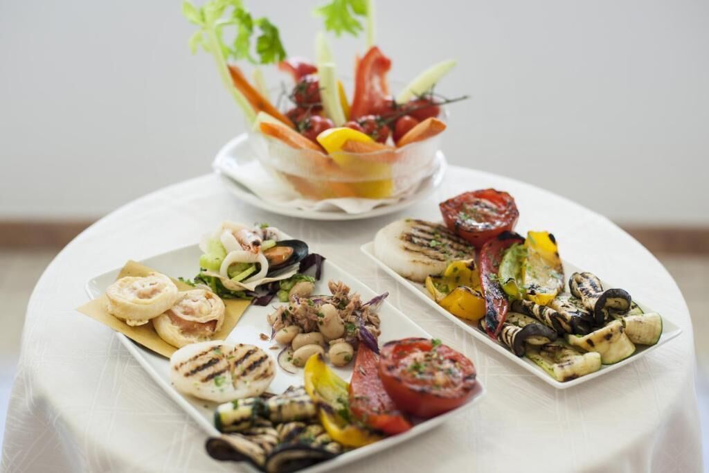 A table with various dishes including grilled vegetables, a salad, and a bowl of mixed fruits and vegetables.