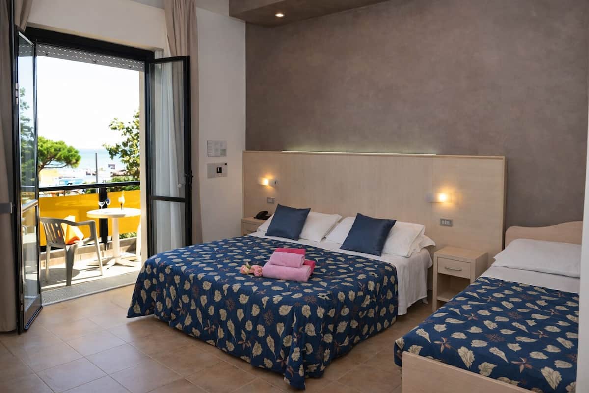 Habitación de hotel con dos camas, un balcón y vista al mar.