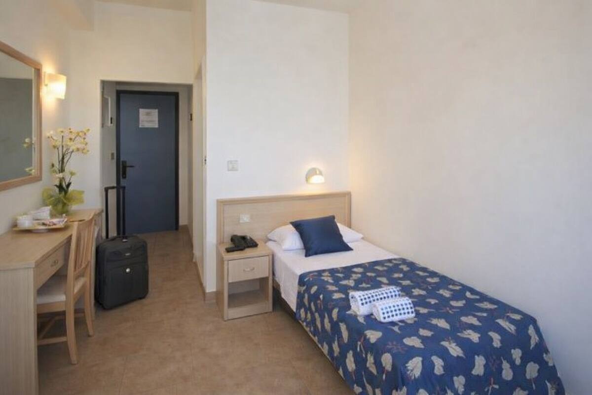 Una habitación de hotel con cama, mesita de noche, lámpara, escritorio, silla y maleta.