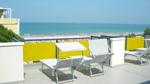 A rooftop terrace with white lounge chairs and a yellow partition, overlooking a beach with a clear blue sky. - Hotel Mimosa (Riccione)