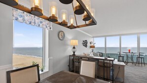 A modern dining area with a view of the ocean, a clock on the wall, and a bar area with seating. - Beachfront Condo/ Pool/ Surfing/ Fishing / EW 1101 (Virginia Beach)