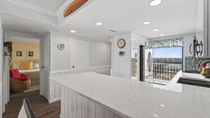 A modern kitchen with a large island, white cabinetry, and a view to the outside. - Beachfront Condo/ Pool/ Surfing/ Fishing / EW 1101 (Virginia Beach)