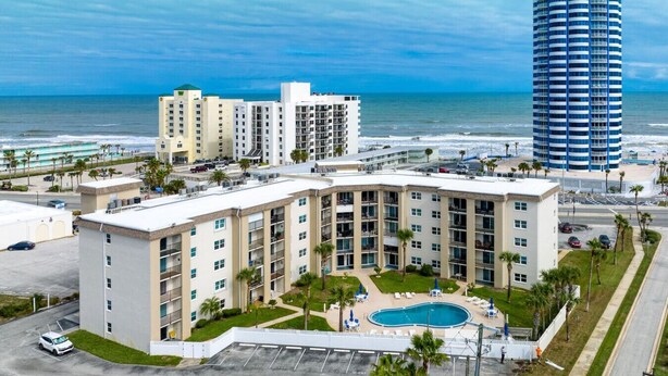 A hotel with a pool, beachfront view, and a tall building nearby. - King`s Getaway Oceanview Pool (Daytona Beach Shores)