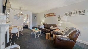 Ein Wohnzimmer mit braunem Ledersofa, einem weißen Couchtisch, einem Esstisch mit Stühlen, einer Pendelleuchte und einem Schild, das die Vermietung von Hütten anzeigt.