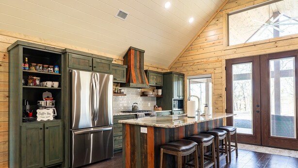 A kitchen with a central island, bar stools, and wooden cabinetry. - Riverfront Retreat | Beach, Fishing & Trails (Broken Bow)