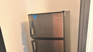 Un refrigerador de acero inoxidable en un rincón de una habitación con piso negro y paredes blancas.