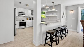 A modern kitchen with white cabinets, a stainless steel oven, and a bar area with stools. - C-View Florida: Canal Front Home w/ Dock! (Anna Maria)