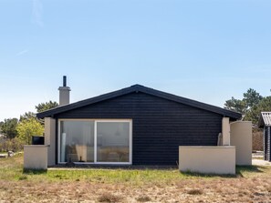 Een modern huis met een donkere gevel, een grote schuifdeur van glas en een schoorsteen.