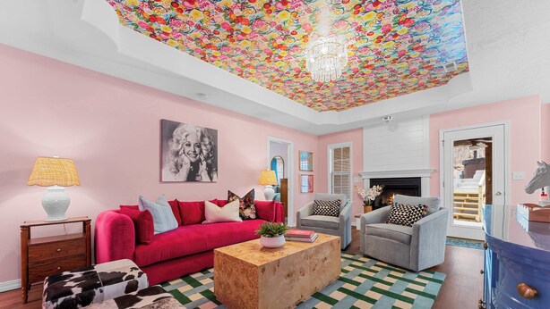 Ein Wohnzimmer mit rosa Wand, einem roten Sofa, einem Holztisch und einem gemusterten Teppich.