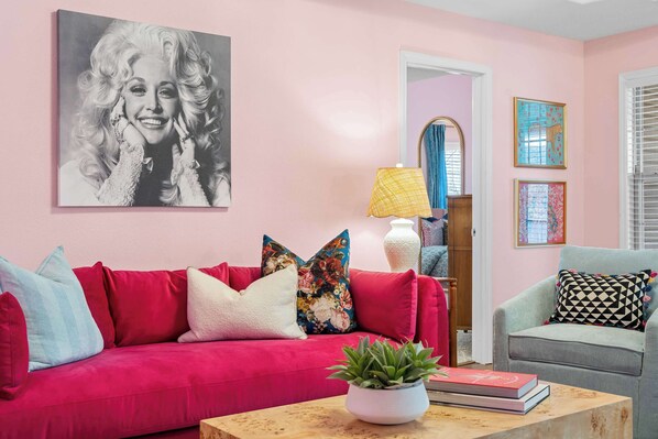 A pink-walled room with a red sofa, a grey armchair, and a coffee table with a plant and books. - Dolly's House! In the heart of Branson! (Branson)