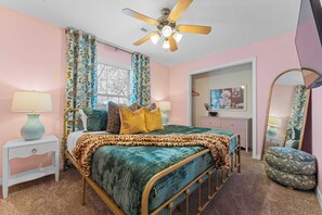 A bedroom with a bed, two bedside tables, a ceiling fan, a window with curtains, a dresser, a mirror, and a door leading to another room. - Dolly's House! In the heart of Branson! (Branson)