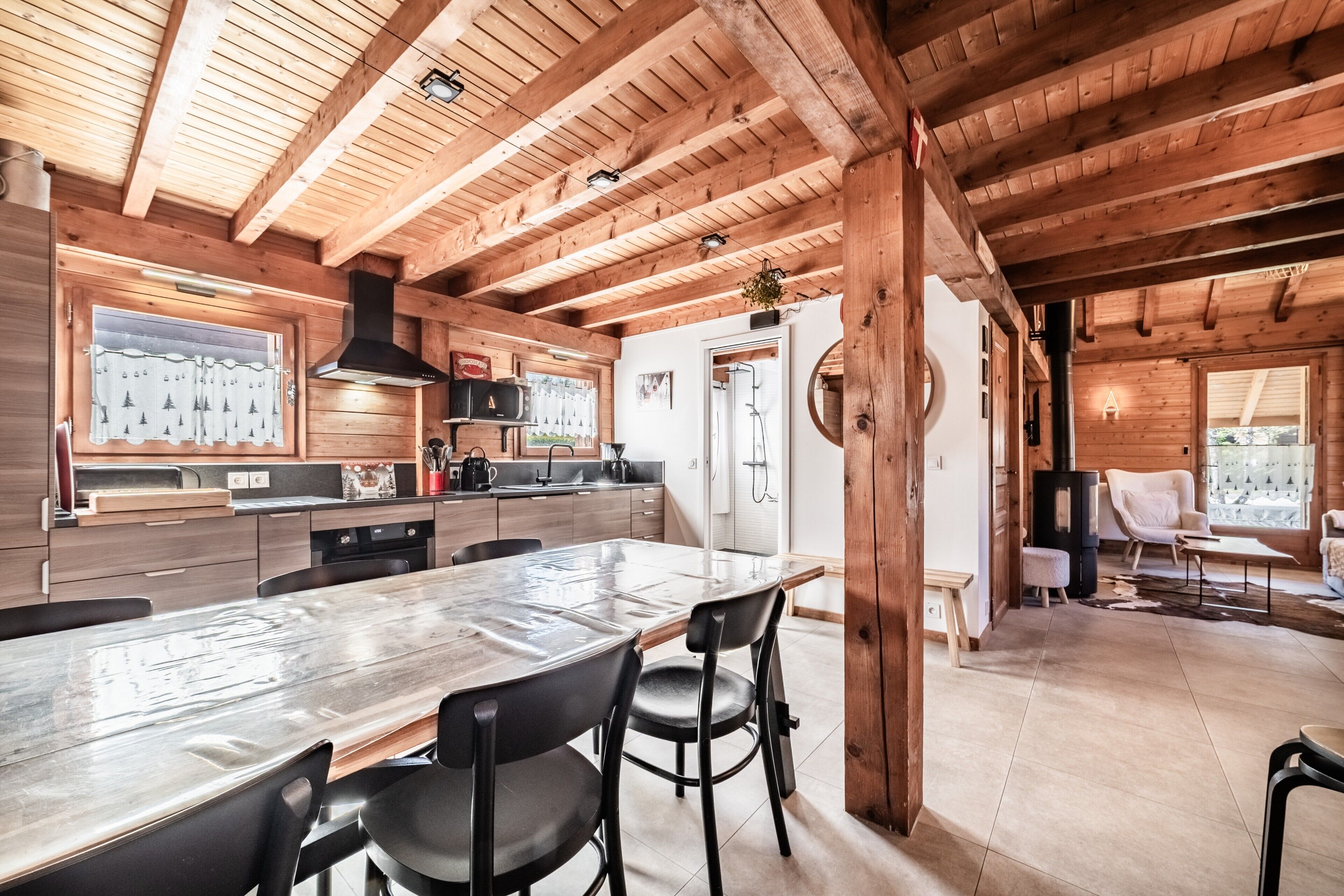 Interior de una cabaña de madera con una gran mesa de comedor, zona de cocina y un rincón de estar acogedor.